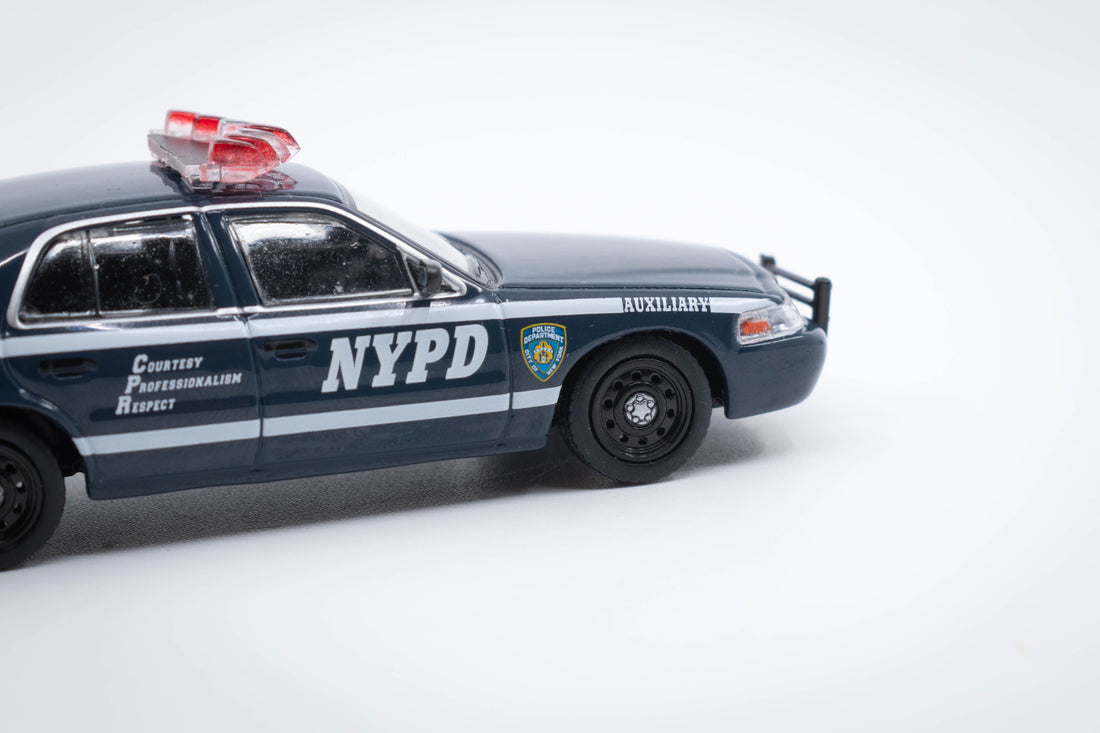 1:64 scale Ford Crown Victoria NYPD Auxiliary diecast model, featuring accurate police graphics, rooftop light bar, and detailed navy blue livery