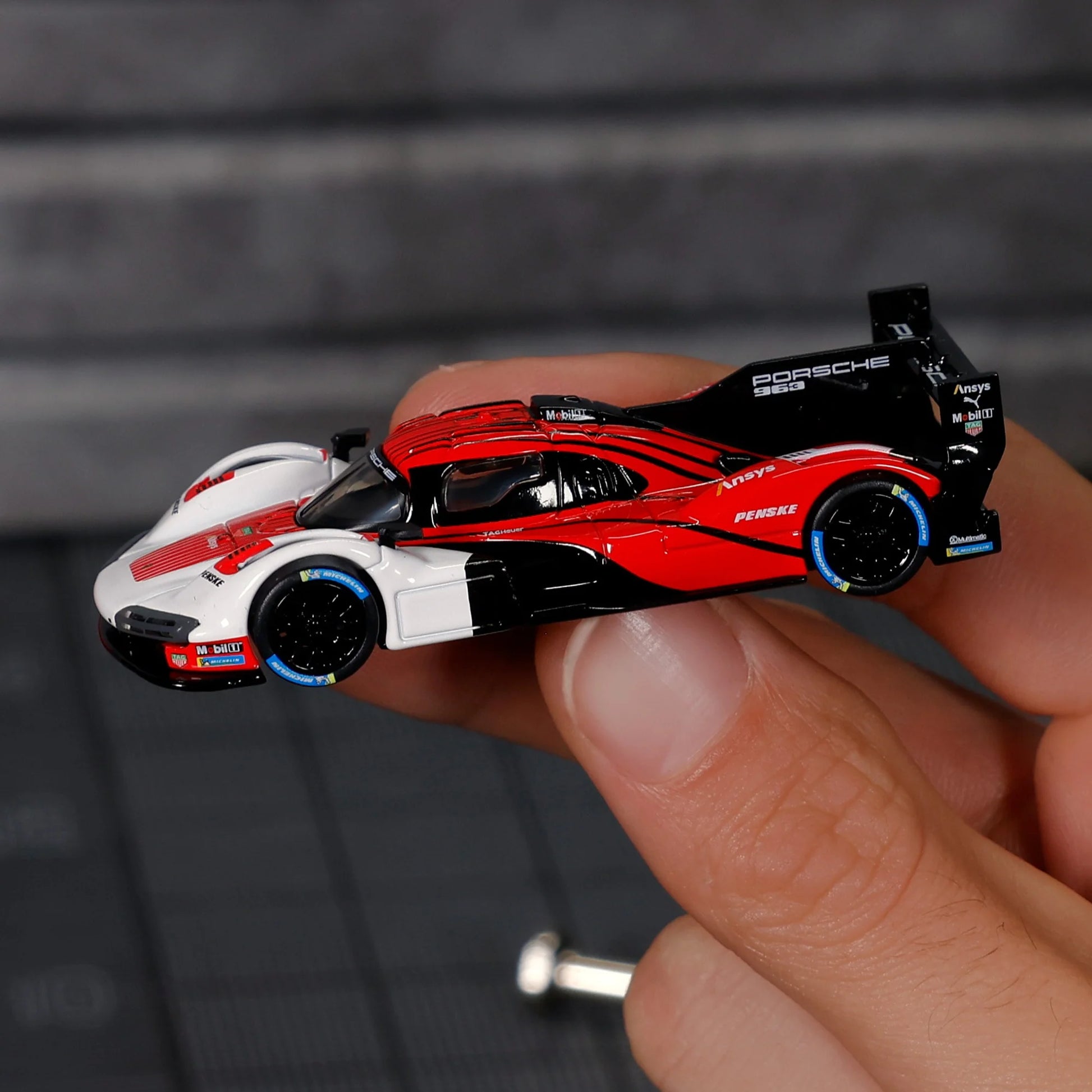 Hot Wheels Elite 64 Porsche 963 in Penske Team livery, featuring red, white, and black racing colors, detailed aero bodywork, and Real Riders wheels.