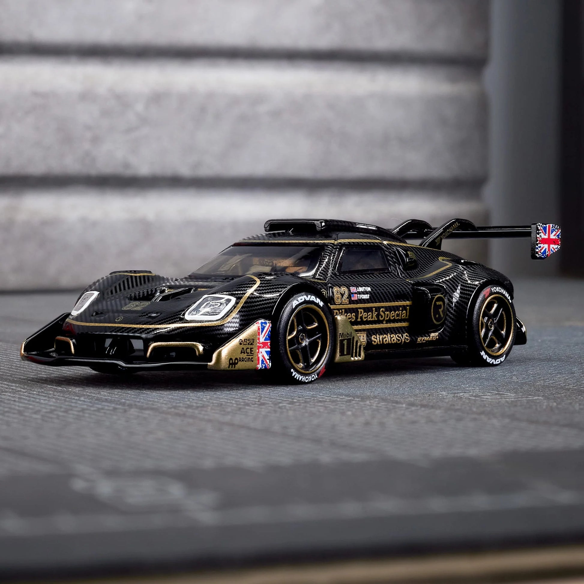 Hot Wheels Elite 64 Radford Type 62-2 Pikes Peak in black and gold JPS livery, featuring aerodynamic bodywork, gold Real Riders wheels, and fine race detailing.