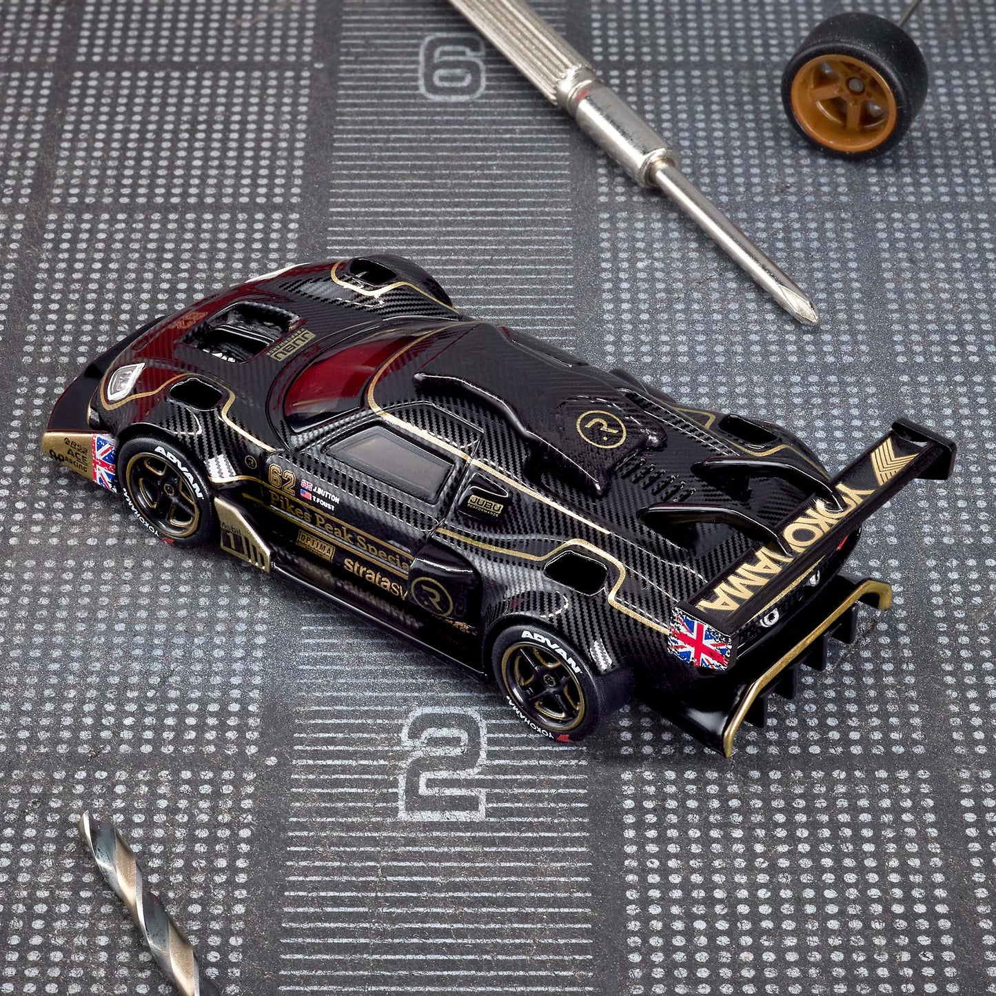 Hot Wheels Elite 64 Radford Type 62-2 Pikes Peak in black and gold JPS livery, featuring aerodynamic bodywork, gold Real Riders wheels, and fine race detailing.