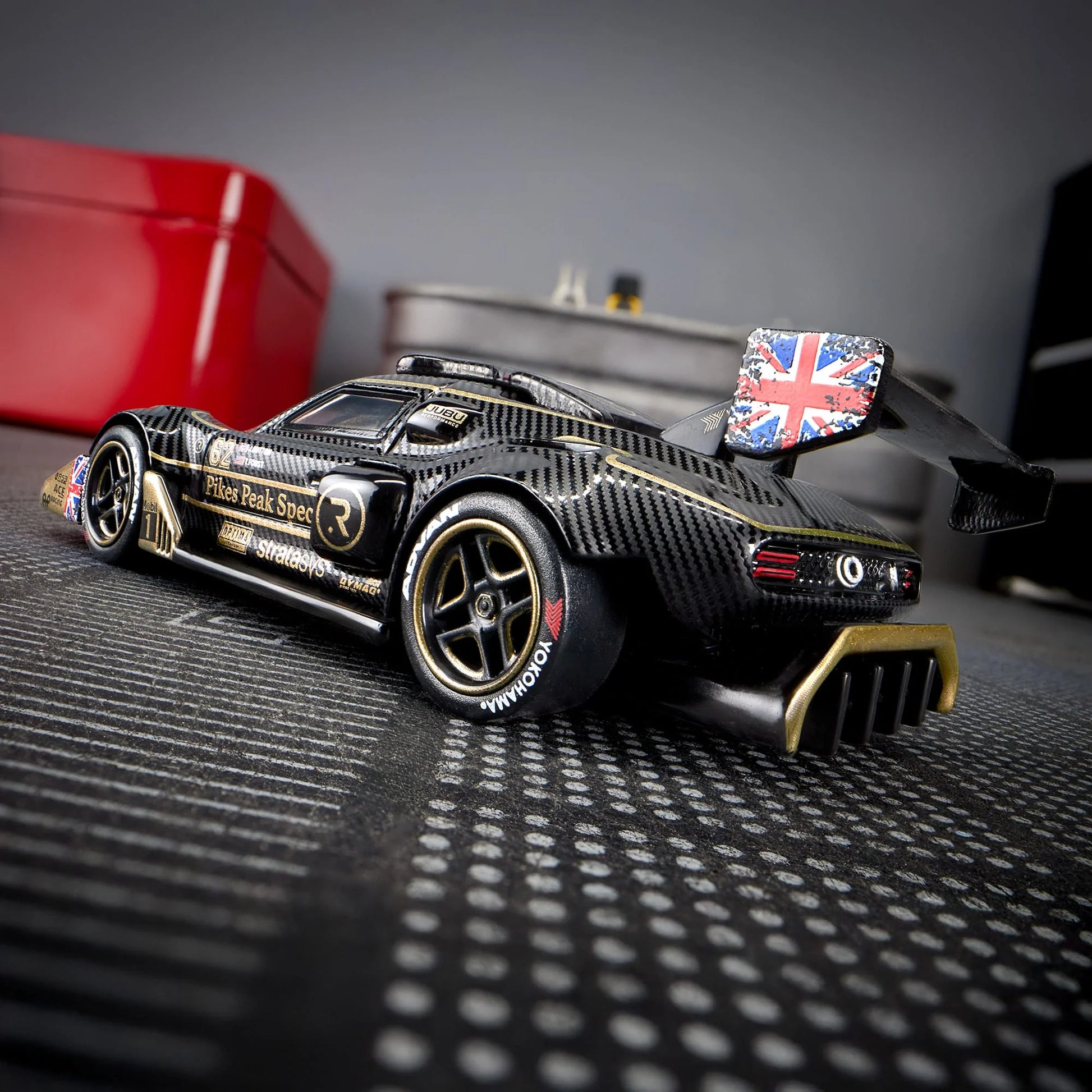 Hot Wheels Elite 64 Radford Type 62-2 Pikes Peak in black and gold JPS livery, featuring aerodynamic bodywork, gold Real Riders wheels, and fine race detailing.