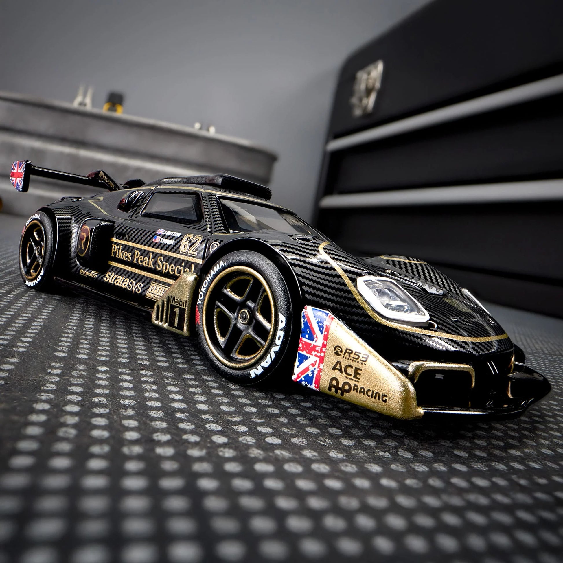 Hot Wheels Elite 64 Radford Type 62-2 Pikes Peak in black and gold JPS livery, featuring aerodynamic bodywork, gold Real Riders wheels, and fine race detailing.
