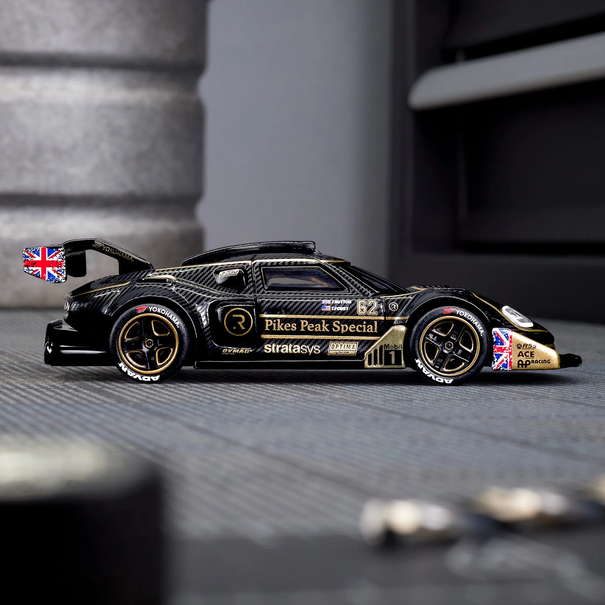 Hot Wheels Elite 64 Radford Type 62-2 Pikes Peak in black and gold JPS livery, featuring aerodynamic bodywork, gold Real Riders wheels, and fine race detailing.
