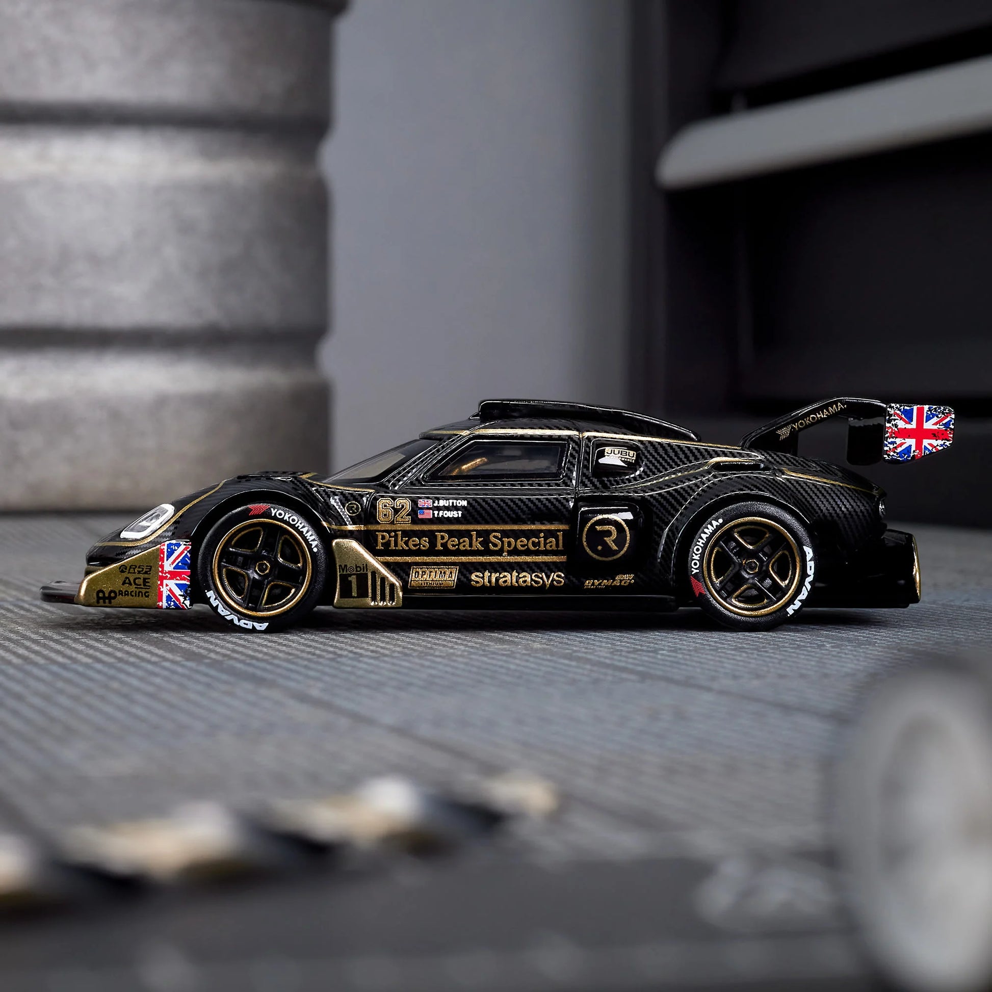 Hot Wheels Elite 64 Radford Type 62-2 Pikes Peak in black and gold JPS livery, featuring aerodynamic bodywork, gold Real Riders wheels, and fine race detailing.