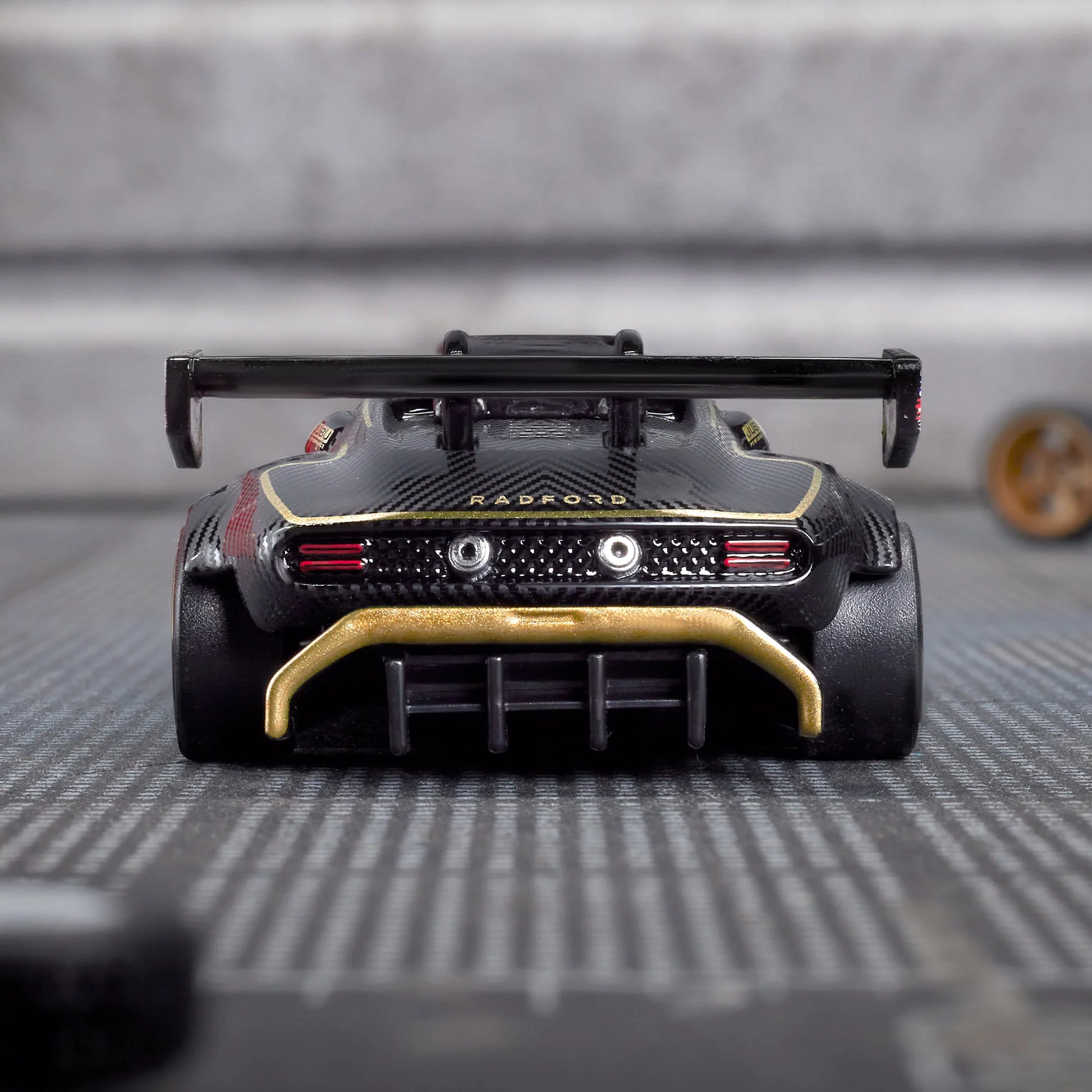 Hot Wheels Elite 64 Radford Type 62-2 Pikes Peak in black and gold JPS livery, featuring aerodynamic bodywork, gold Real Riders wheels, and fine race detailing.