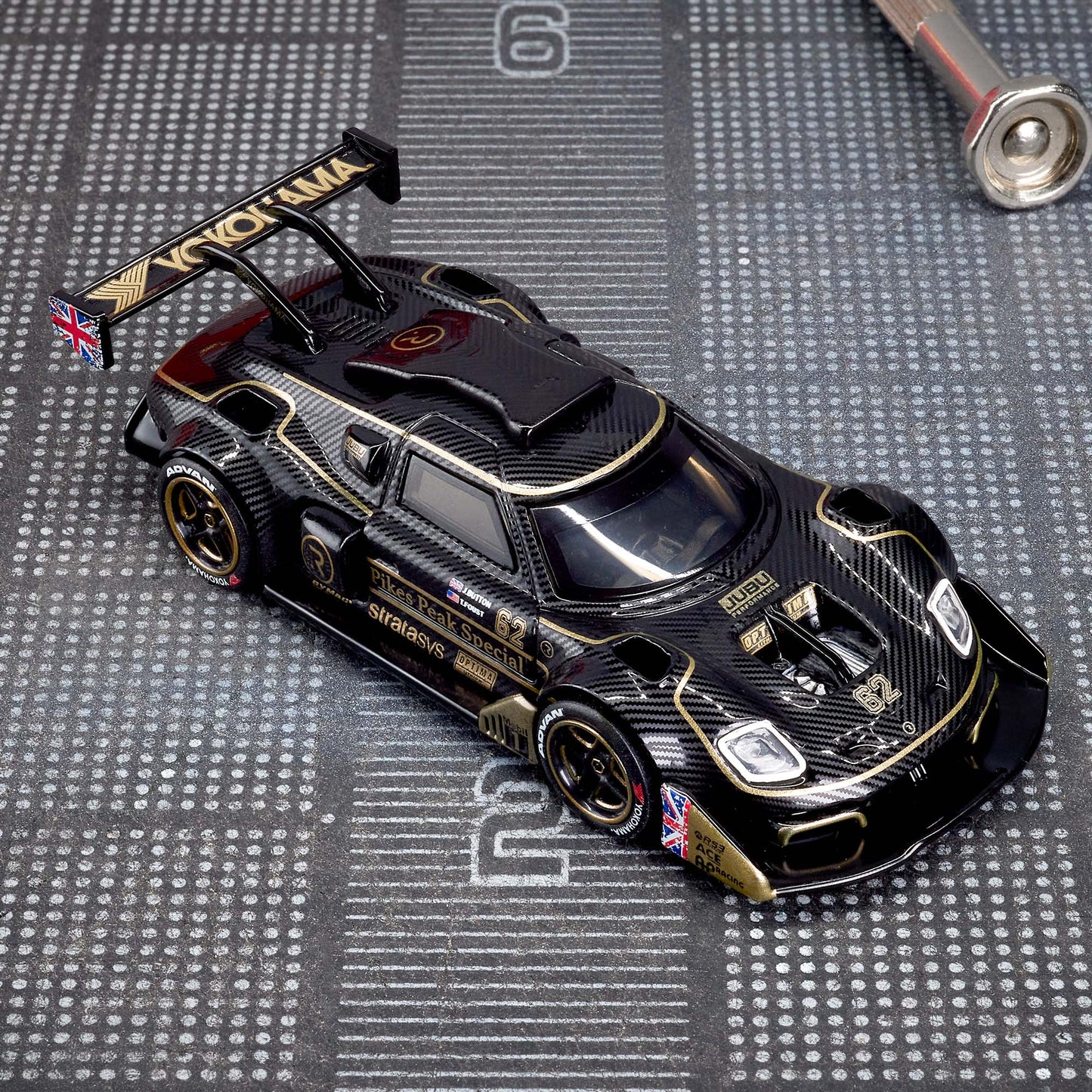 Hot Wheels Elite 64 Radford Type 62-2 Pikes Peak in black and gold JPS livery, featuring aerodynamic bodywork, gold Real Riders wheels, and fine race detailing.
